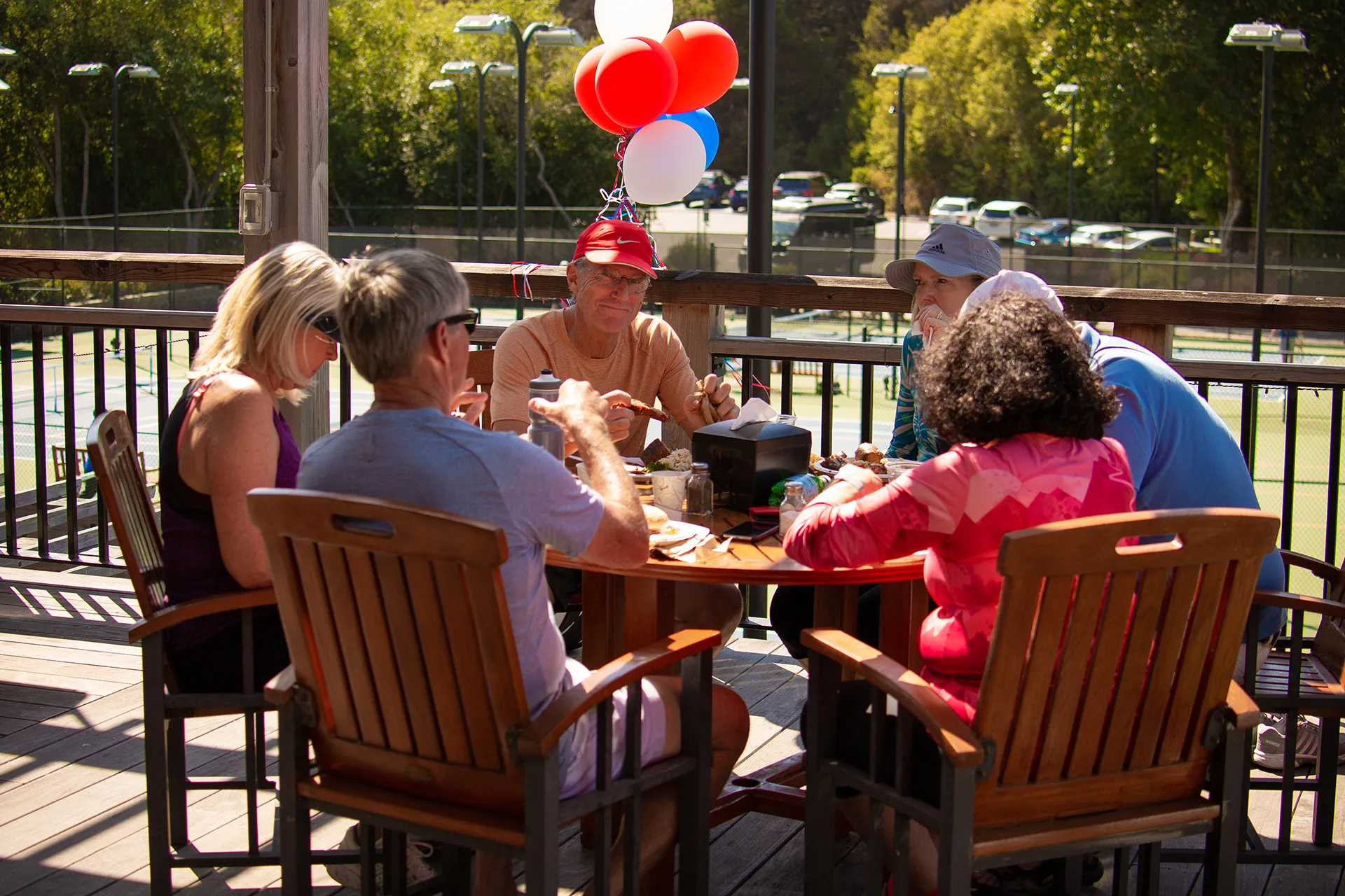 Member smirks at the camera as he eats food on the CVAC deck. Red, white and blue balloons float behind him.