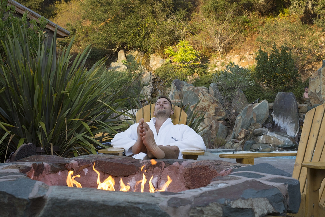 Parent relaxing near a firepit at Refuge spa